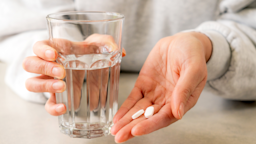 A woman holds two pills in one hand and a glass of water in the other hand.
georgeclerk/iStock via Getty Images Plus