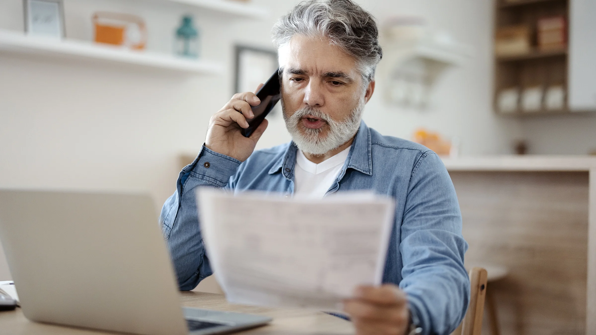 A man holds paperwork while talking on the phone.