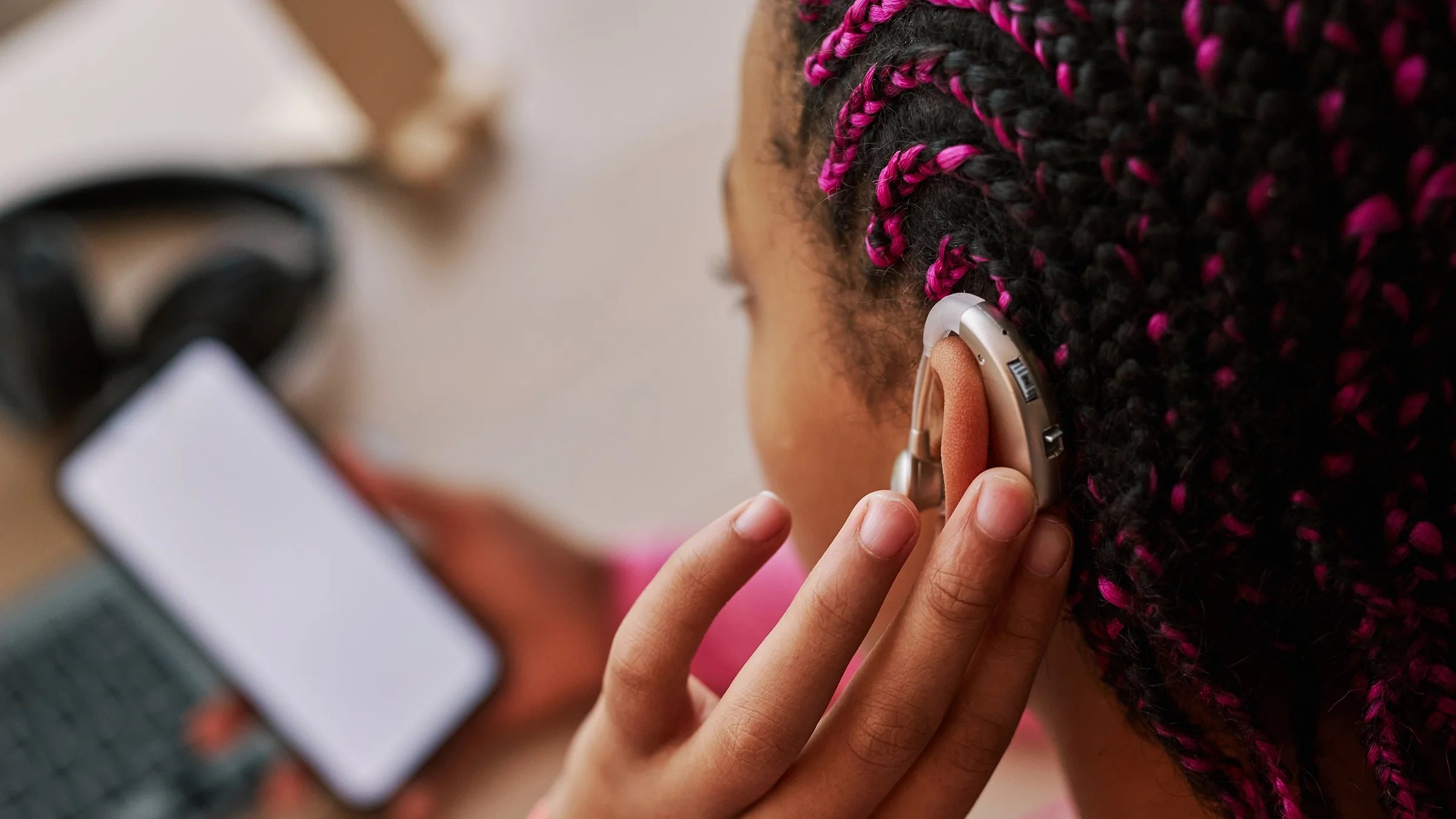 A teenage girl, shown in close-up, wears a hearing aid on her ear.
