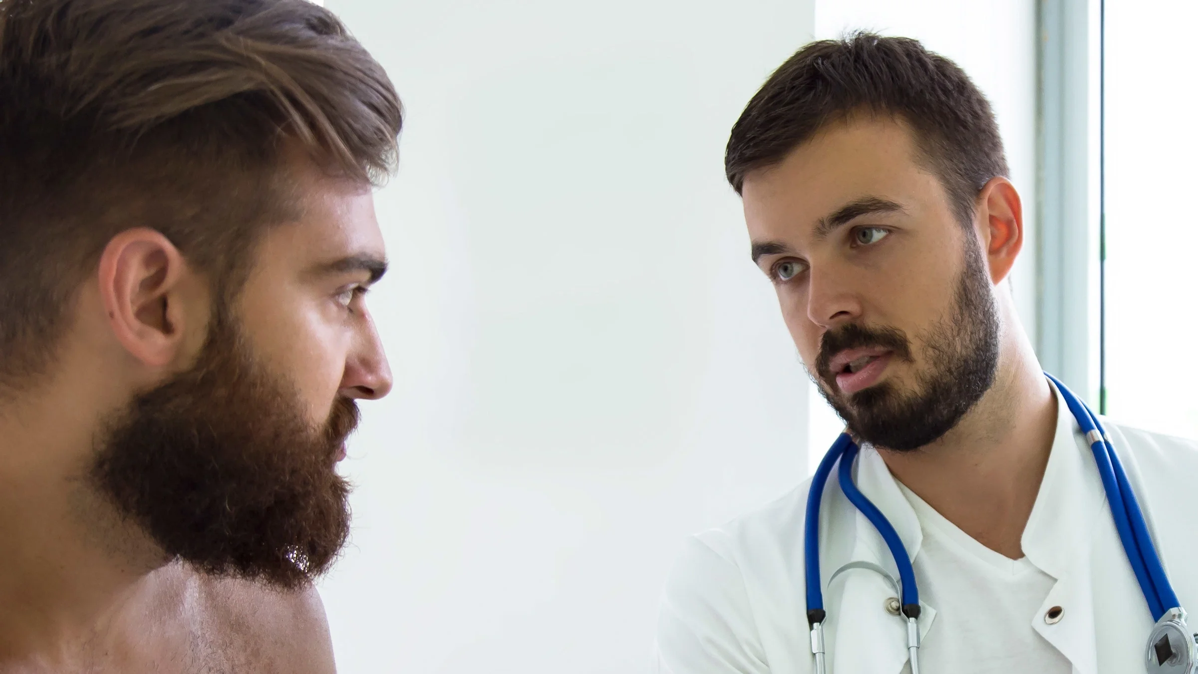 A shirtless patient talking to a doctor.