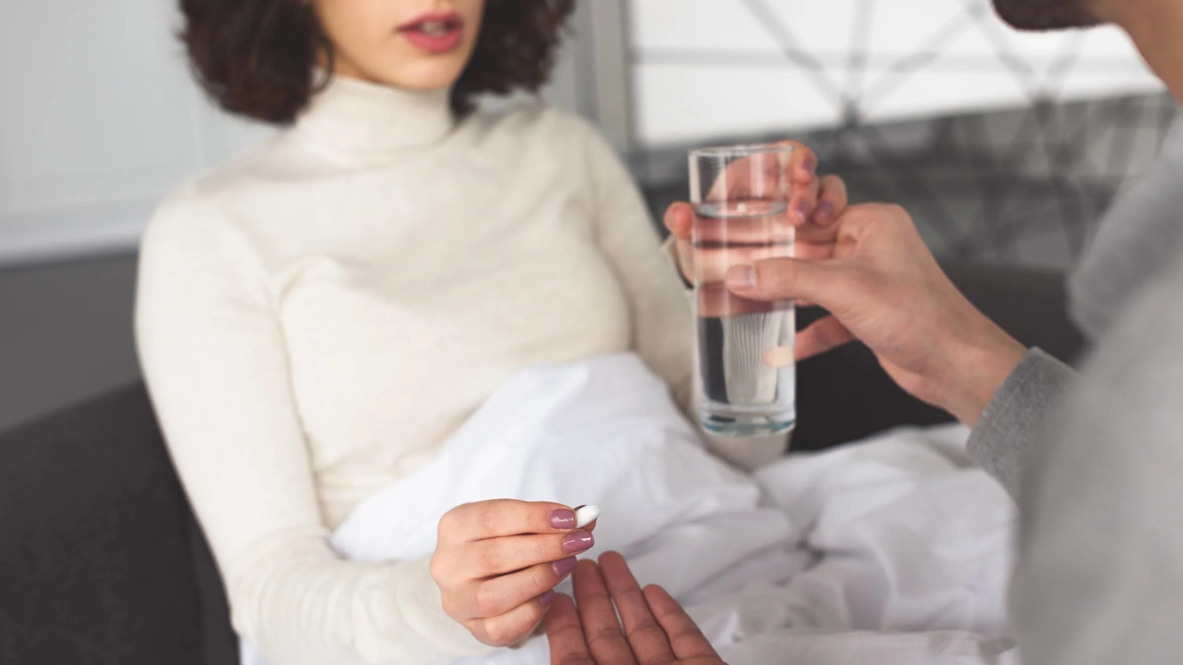 Cropped image of someone being offered a pill and water by their partner.