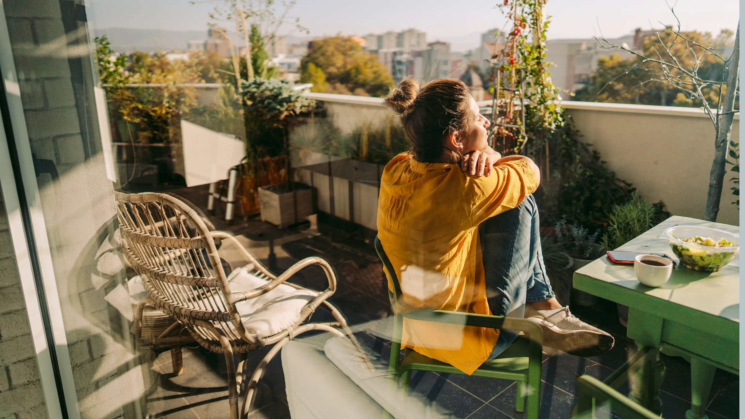 A woman enjoys the morning sun and has coffee on her balcony.