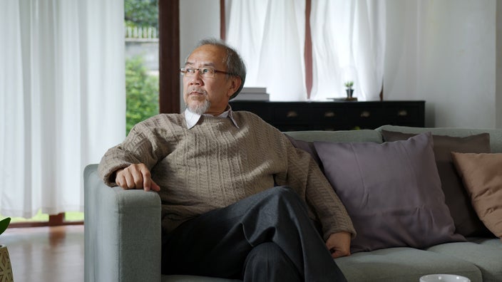 An older man is sitting on a couch and staring off into the distance.