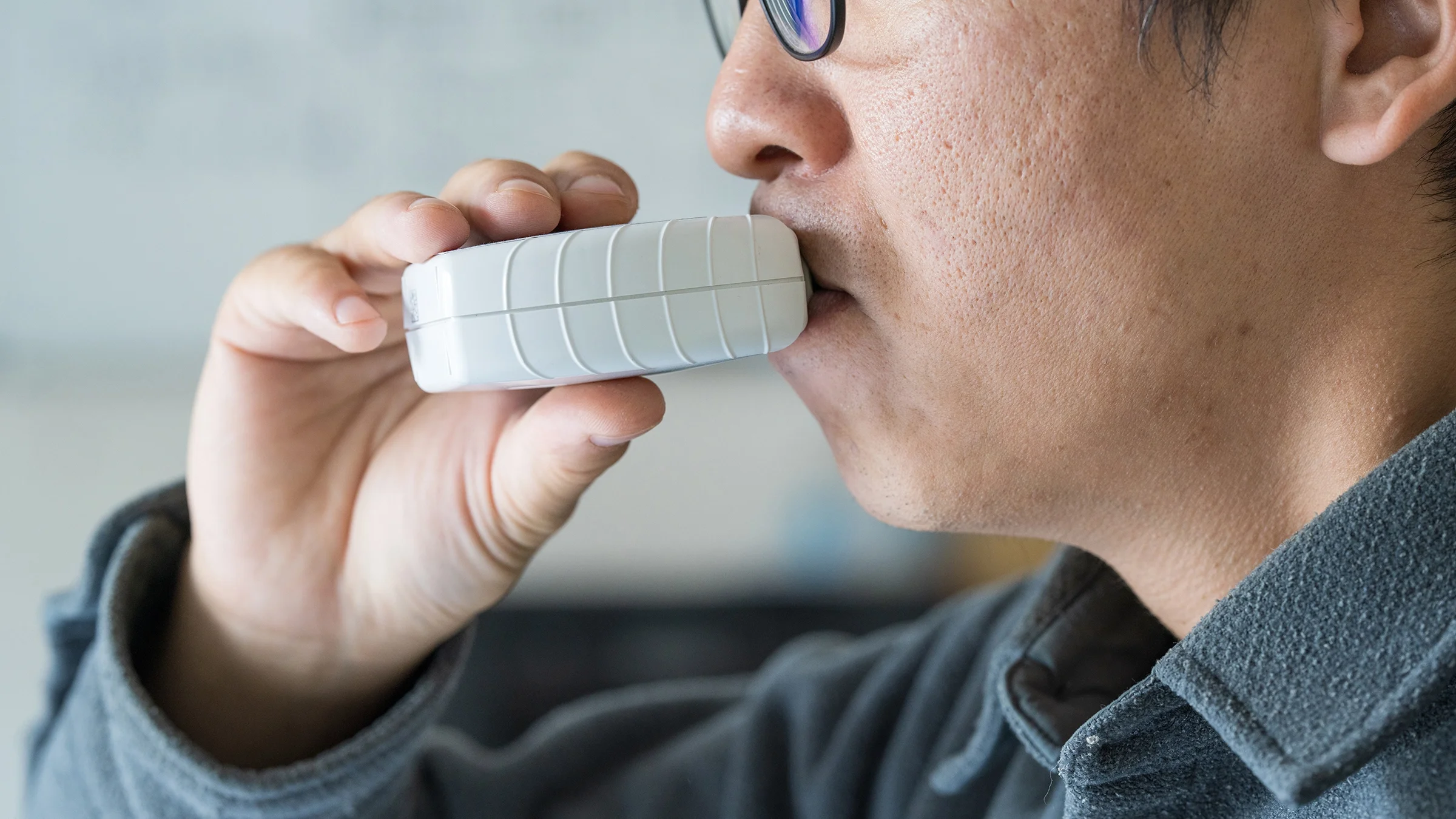 A man is pictured using an asthma inhaler in a close-up.