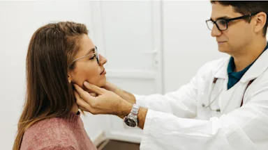 A doctor touching and examining a patient's thyroid glands.
bojanstory/E+ via Getty Images
