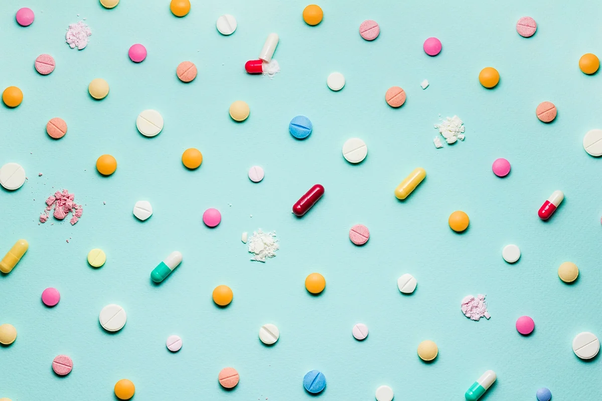 Flat lay image of different types of pills with some crushed on a light teal background.