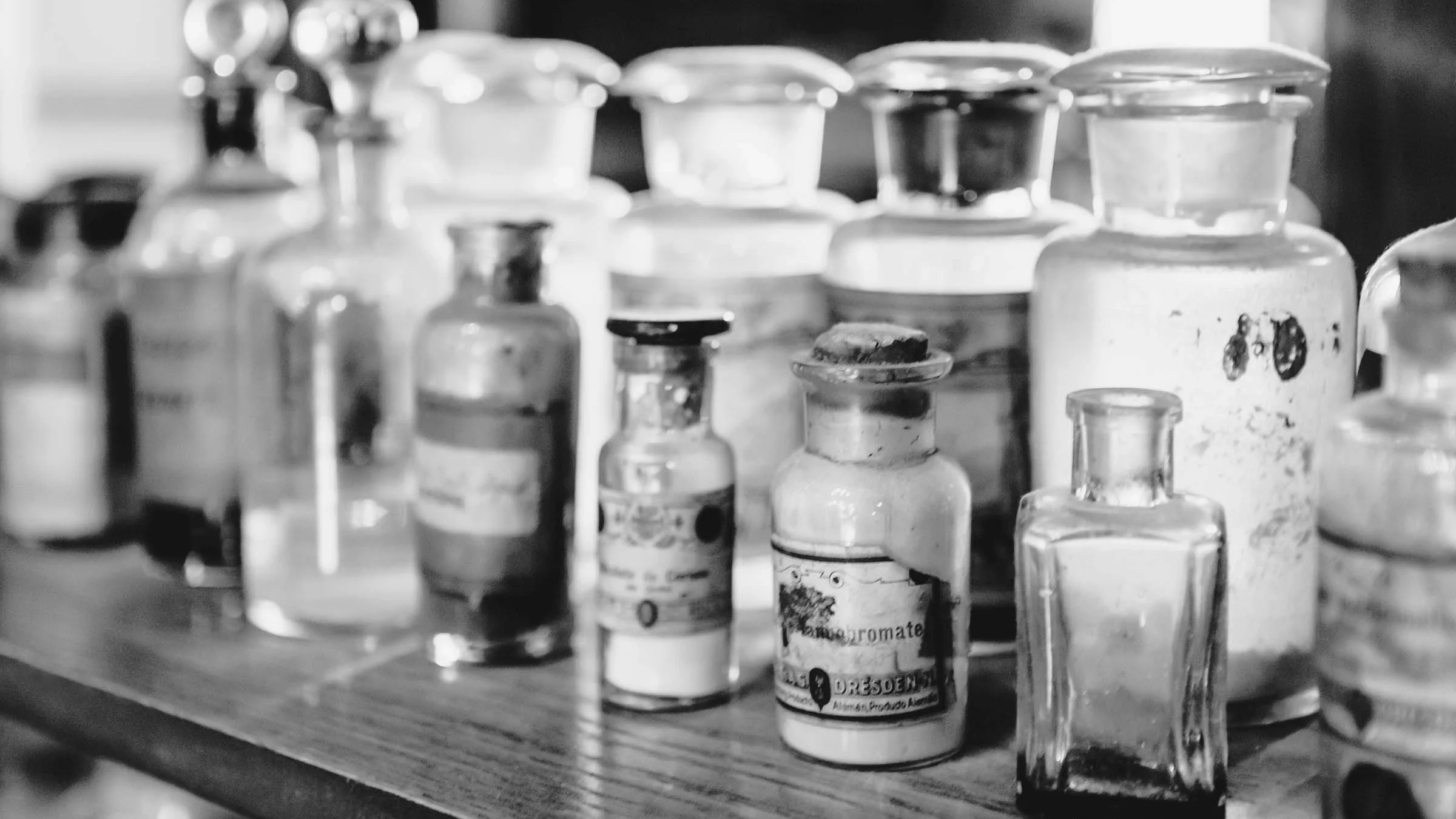 Black and white close-up of old vintage apothecary jars on the shelf.