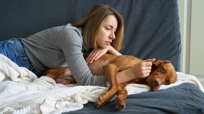 A pet owner lying with her lethargic dog on the couch.