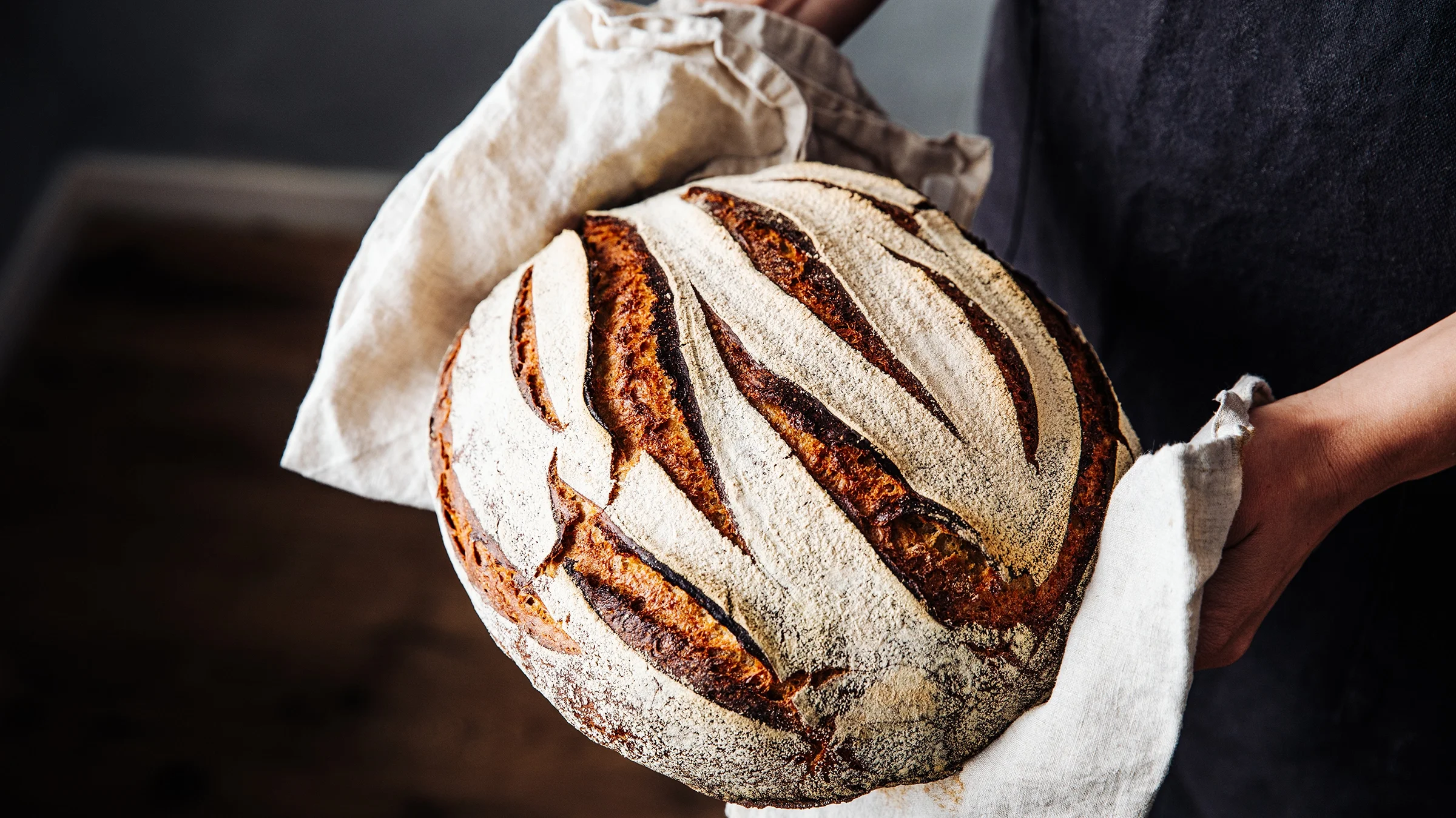 A baker is holding a loaf of freshly baked sourdough bread.