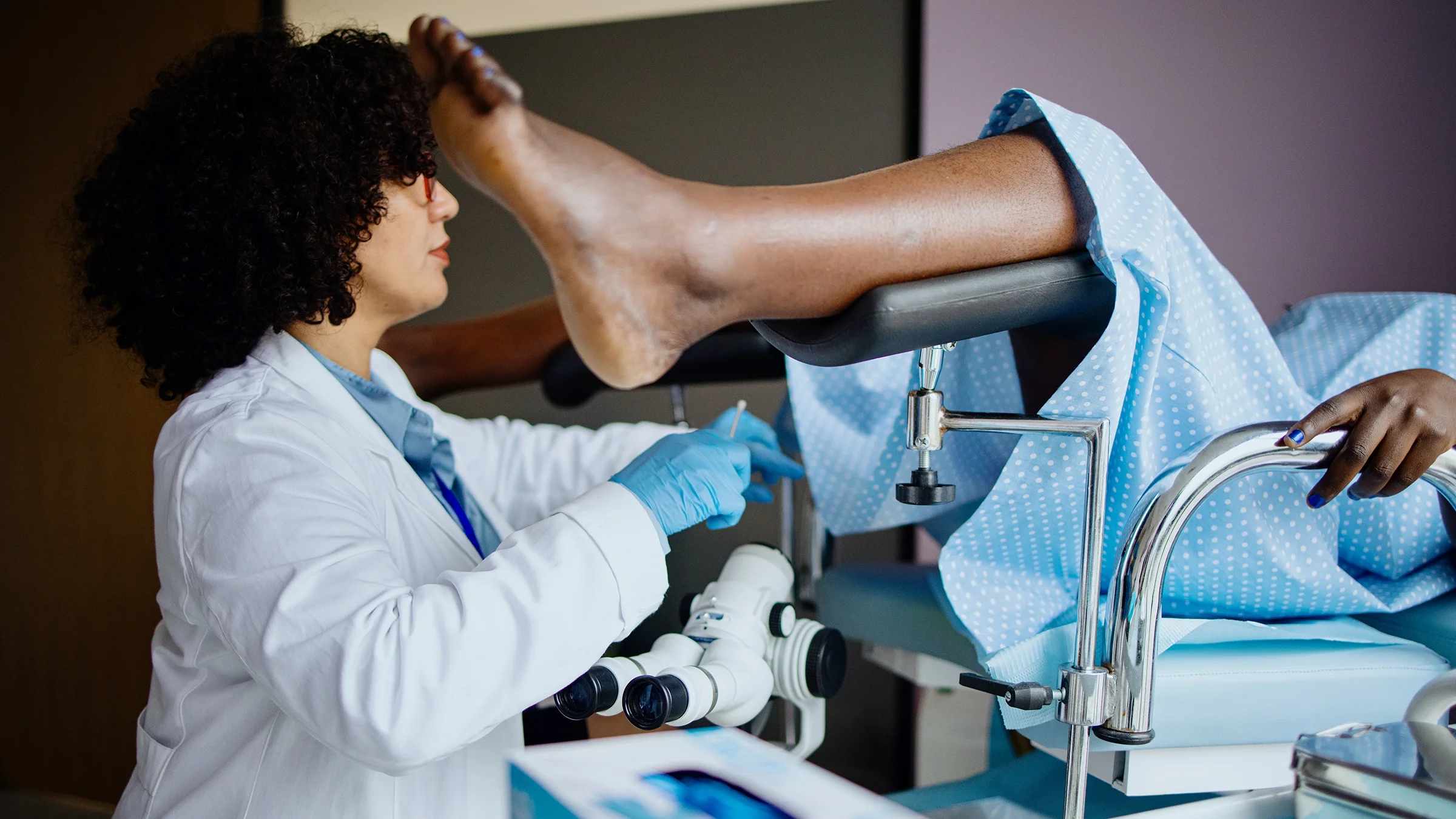 A woman is in a gynecologist’s exam room with her legs in the stirrups.