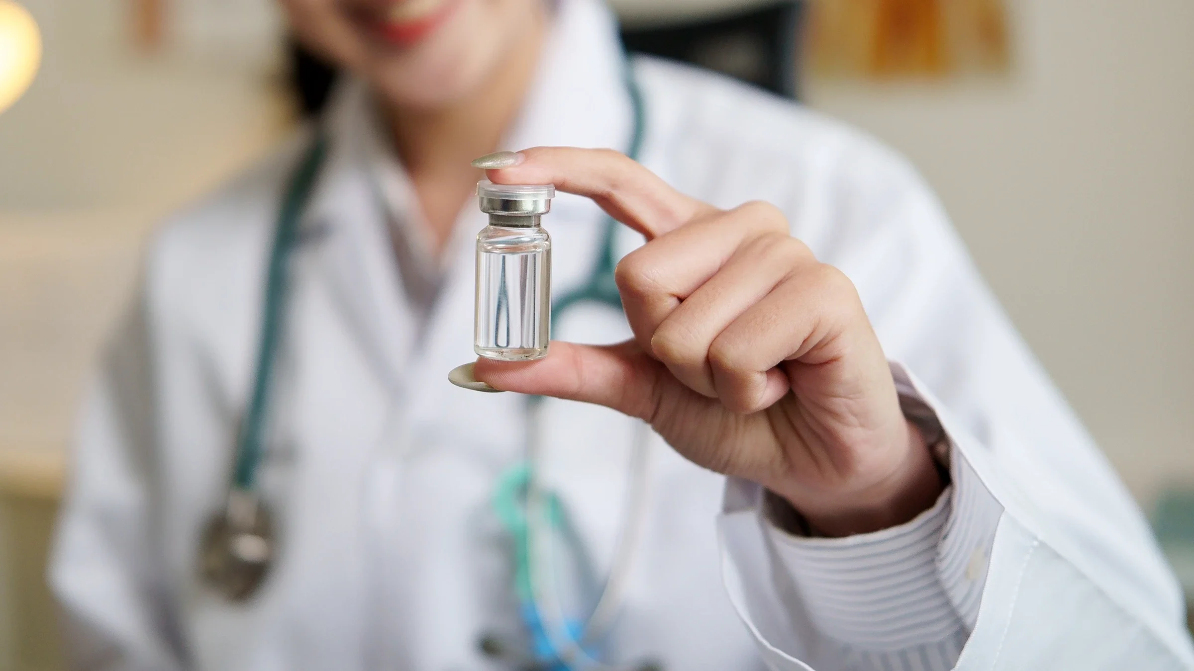 A healthcare professional holds a medical vial between their thumb and forefinger.
