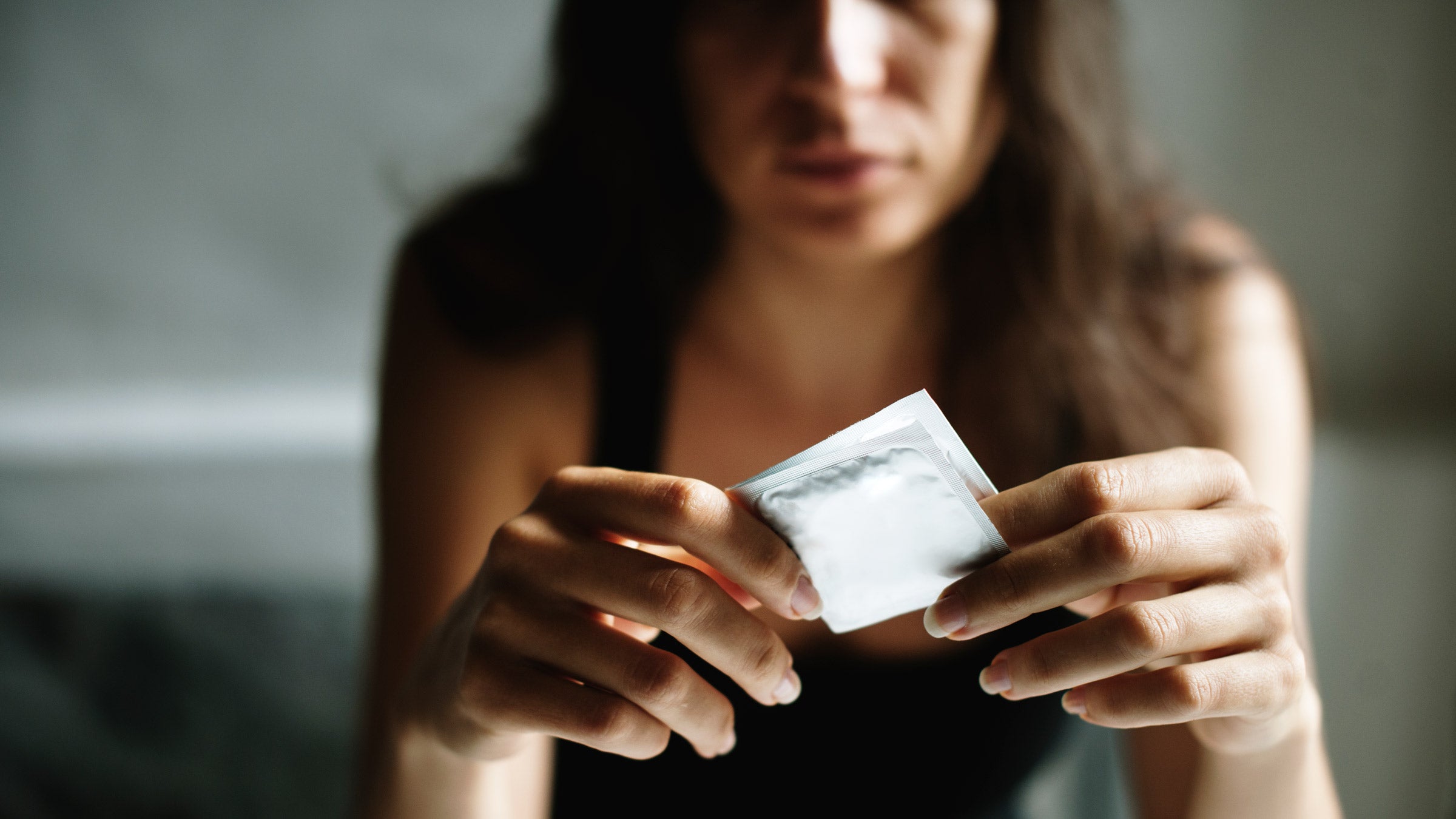 Sexual health: Women: cropped serious expression holding condom-843517818
