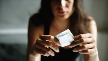 Sexual health: Women: cropped serious expression holding condom-843517818