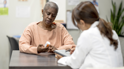 A woman with a prescription bottle in her hand chats with a doctor.
FatCamera/E+ via Getty Images
