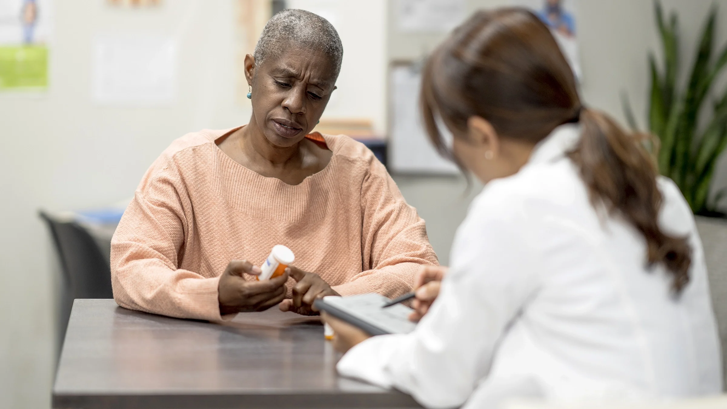 A woman with a prescription bottle in her hand chats with a doctor.