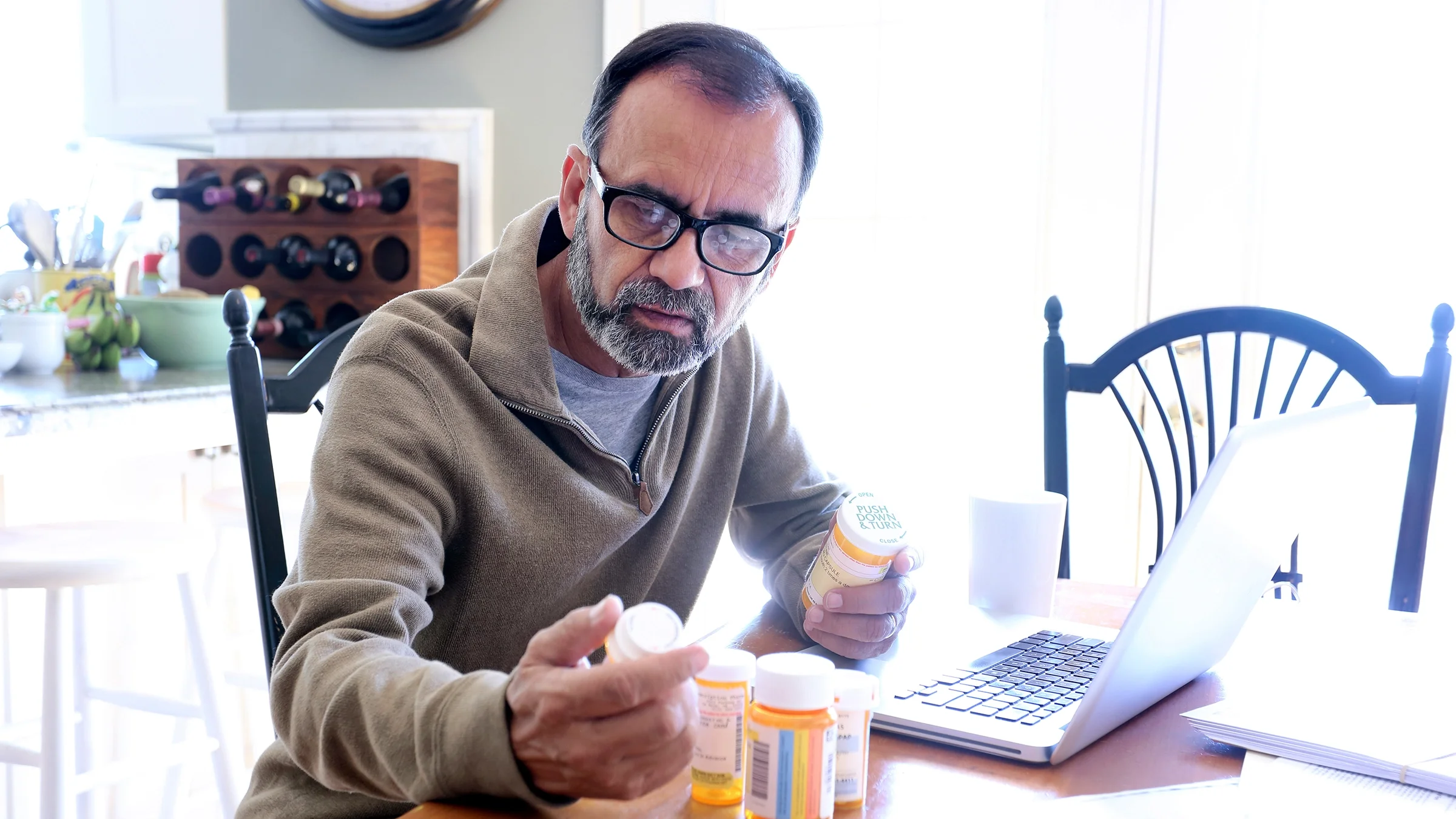 A man is reading the labels of his prescription medication bottles.