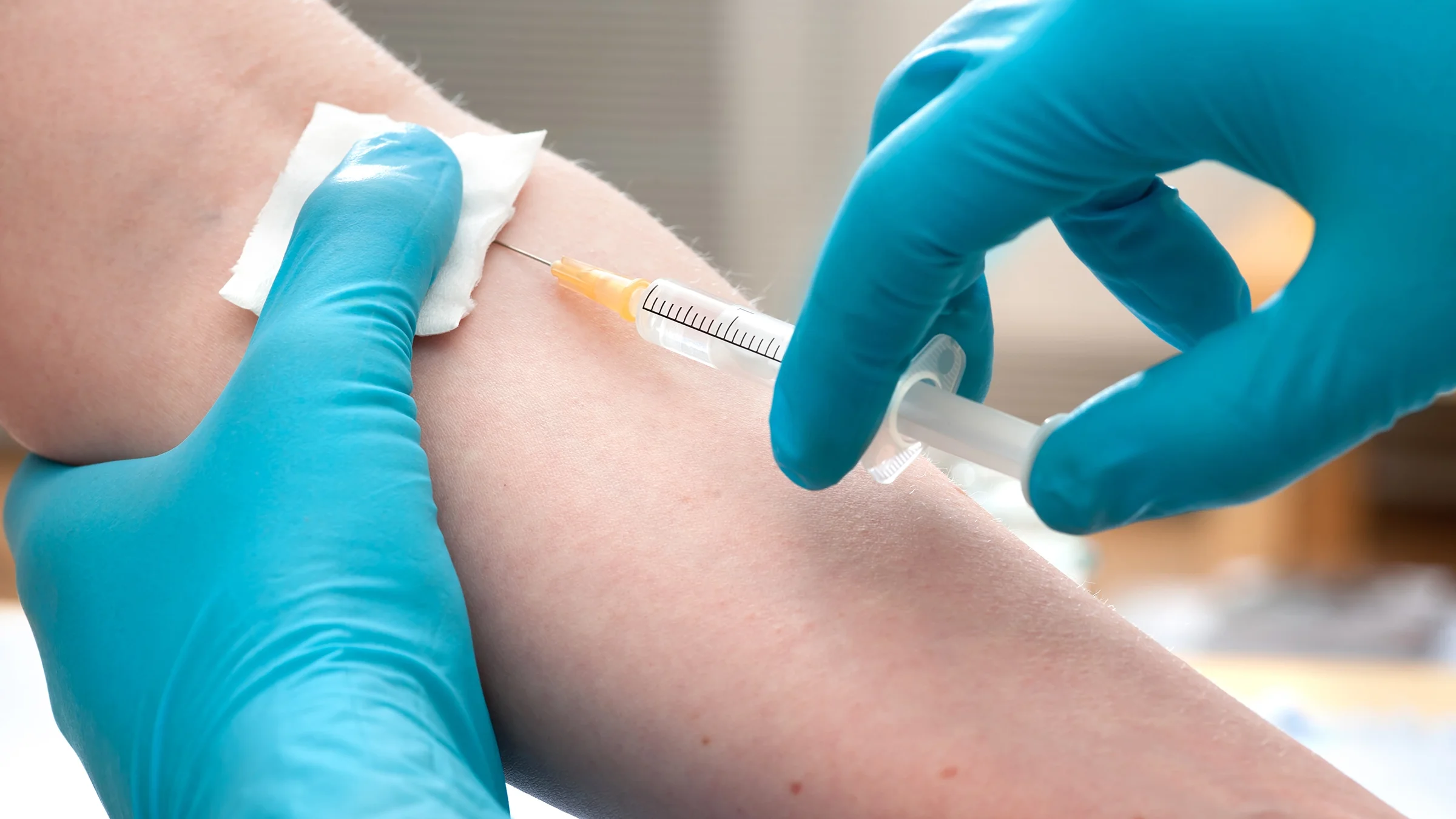 Close-up of a nurse with blue medical gloves giving a person an injection.