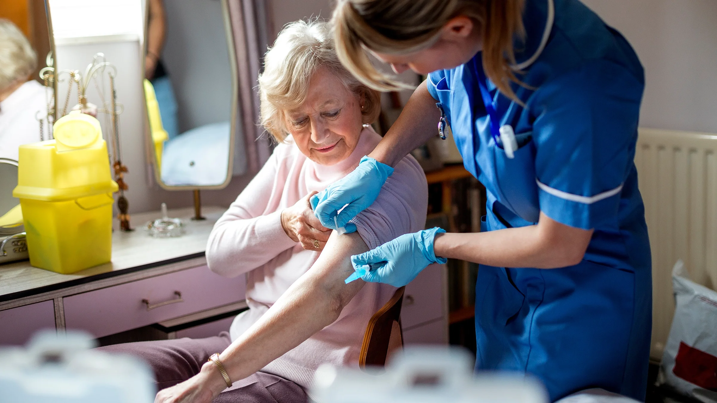 A senior woman receives a vaccination during a home care visit.