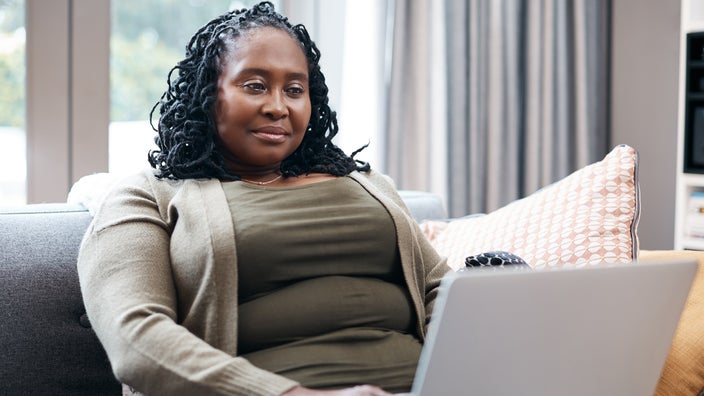 Woman sitting on her couch with her laptop looking something up on the internet. She has a soft smile on her face.