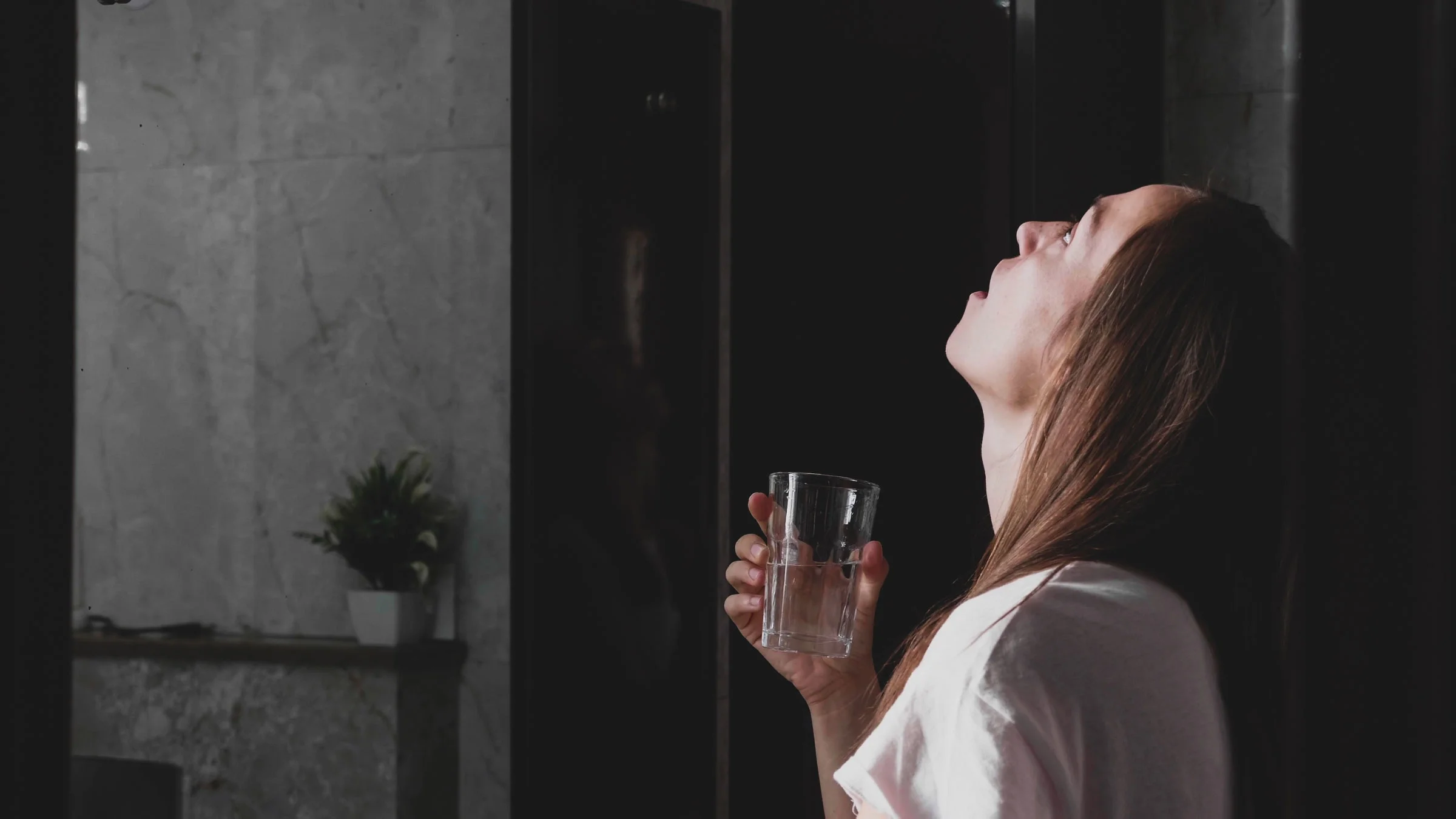 Woman gargling a glass of water in the bathroom.