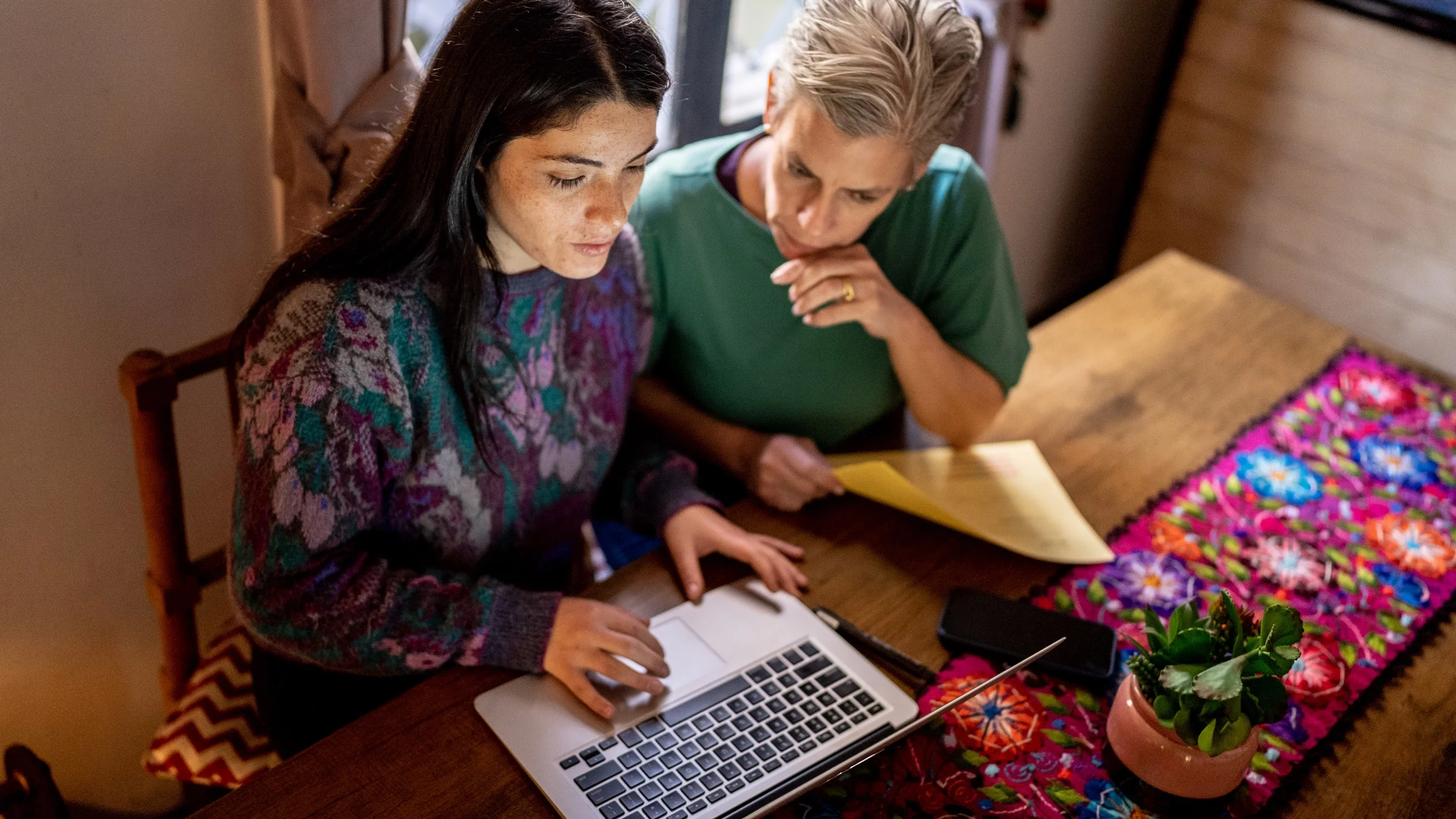 A young adult and their older parent looking at a laptop and documents.