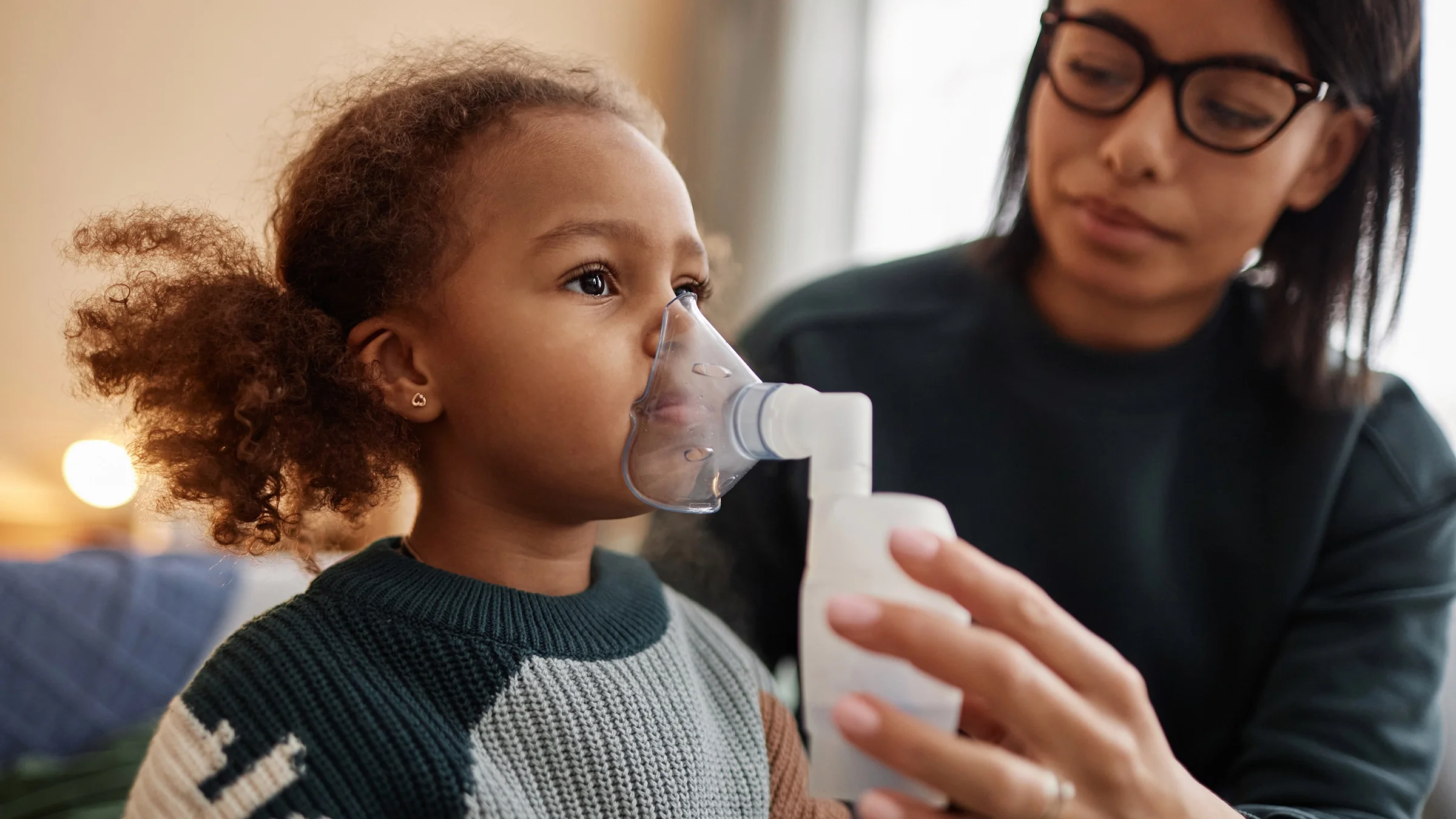 A mother holds a nebulizer to her daughter’s face.