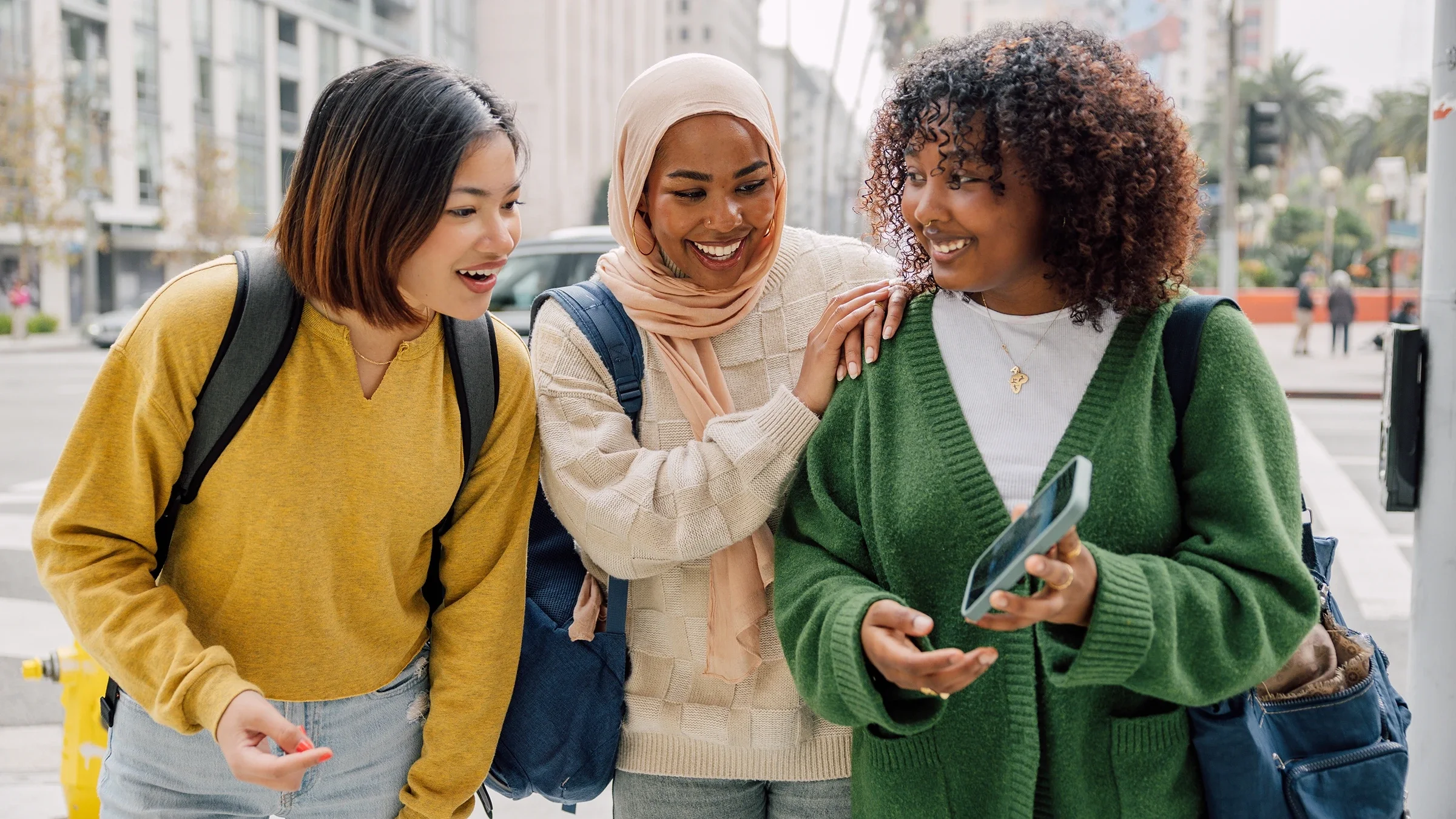 Young women smile as they look at something on a mobile phone screen.