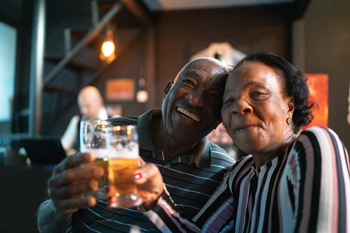 Elderly couple clinking glasses with beer and smiling at home.