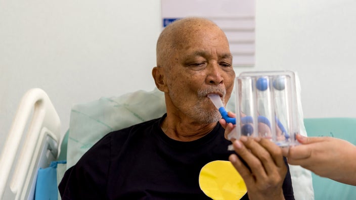 A man uses an incentive spirometer, a device that helps keep lungs fully expanded.