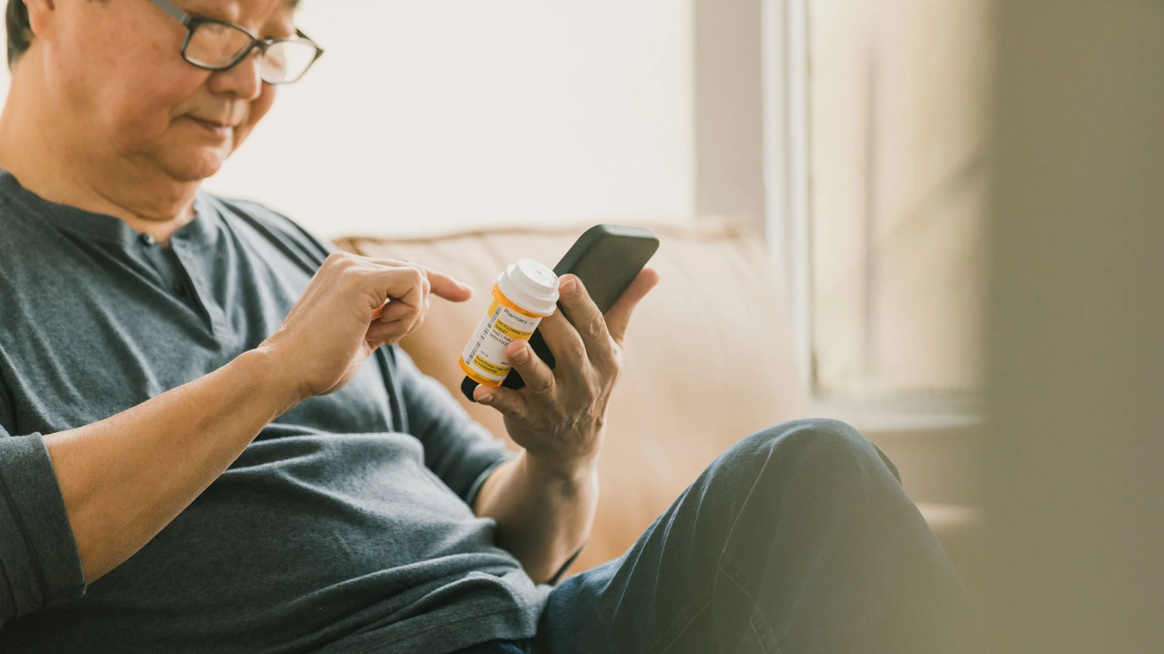 Man holds medicine and phone at home.