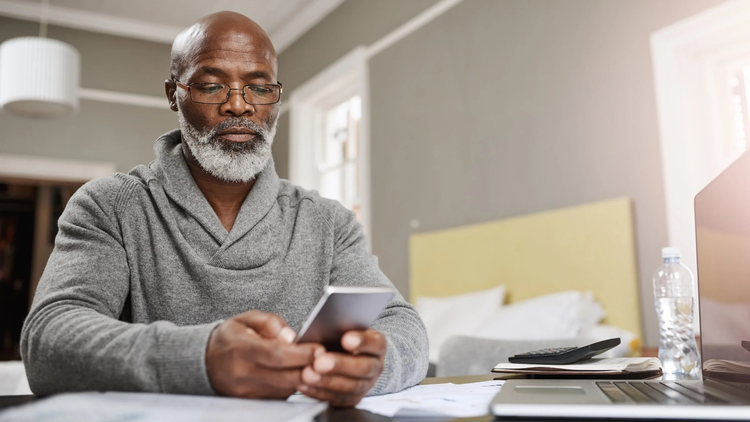 Older man sitting at a table using his smartphone for financial budgeting.
