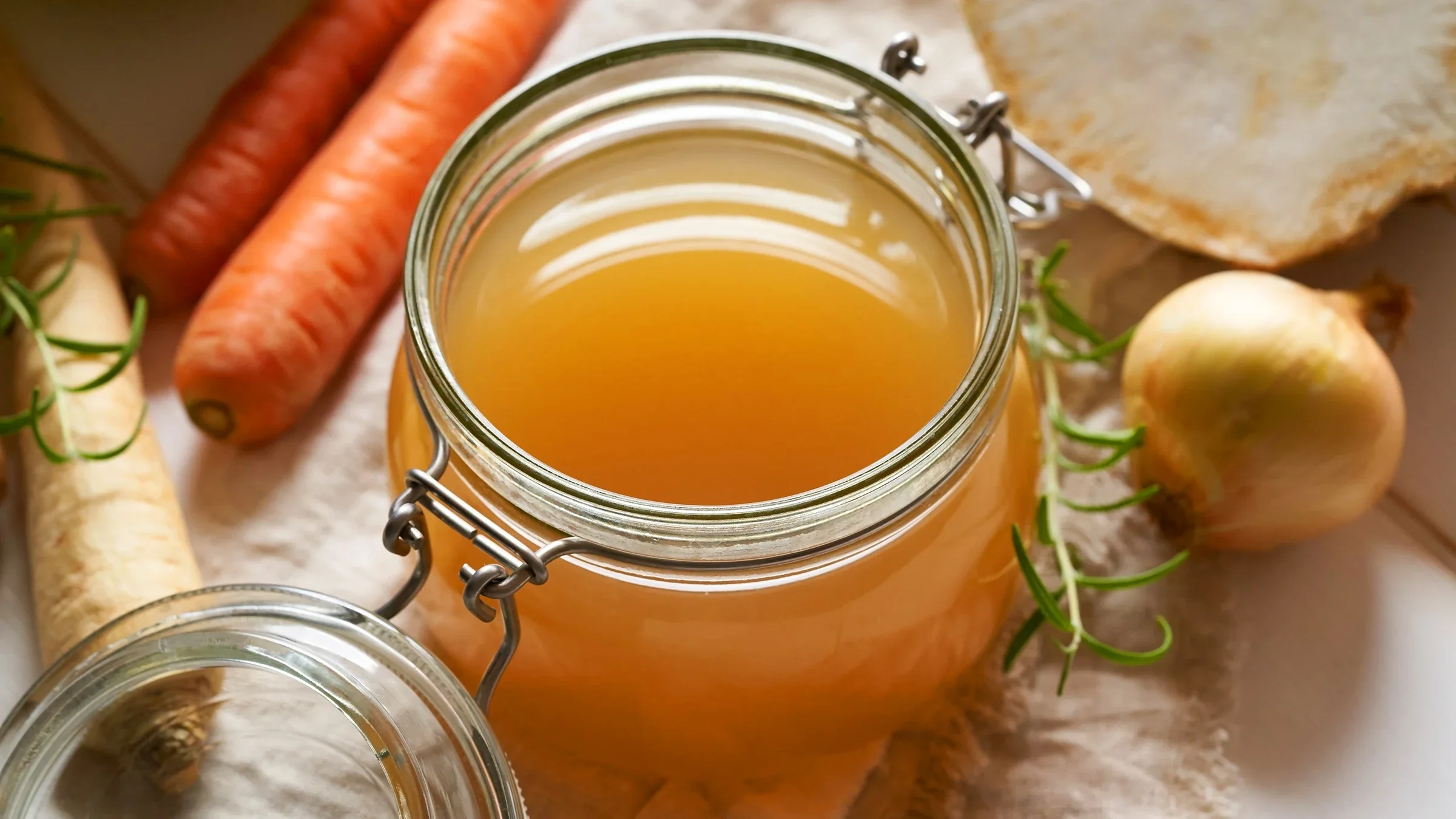 A homemade beef bone broth in a glass jar is pictured. Some carrots, onion, and other vegetables surround it.
Madeleine_Steinbach/iStock via Getty Image Plus