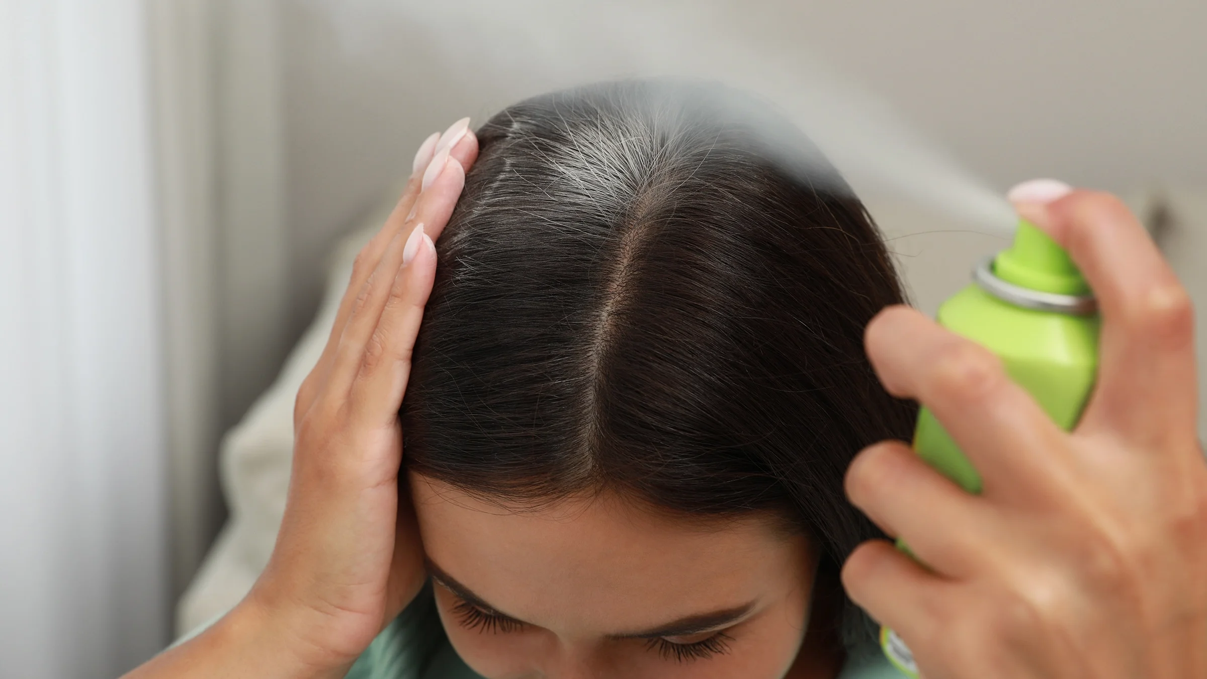 Woman spraying dry shampoo onto her hair.
