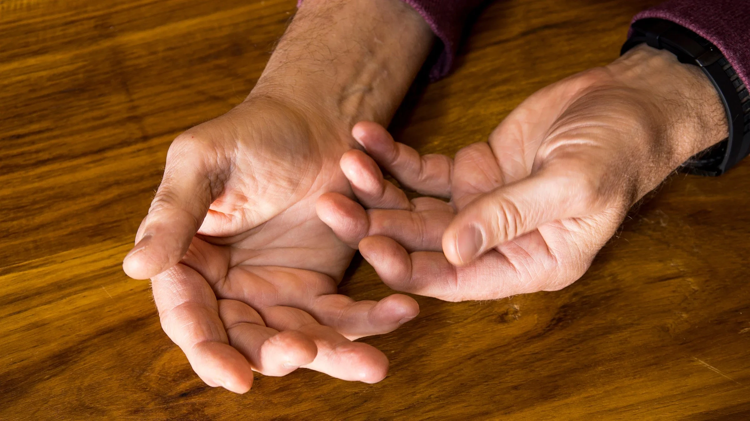 Close-up of a person's arthritic hands on a wooden table background.