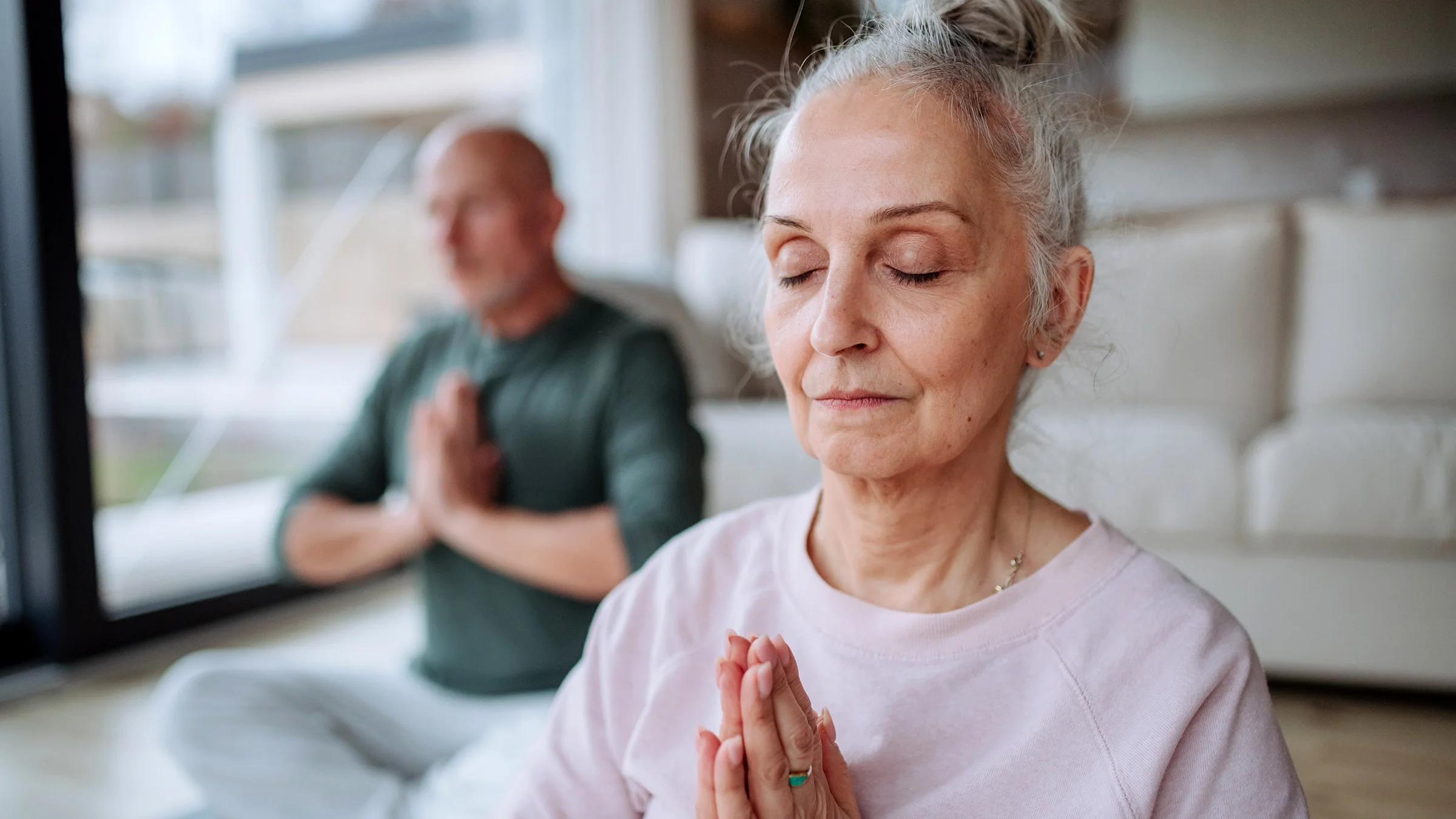 An older couple is doing relaxation exercises together at home.