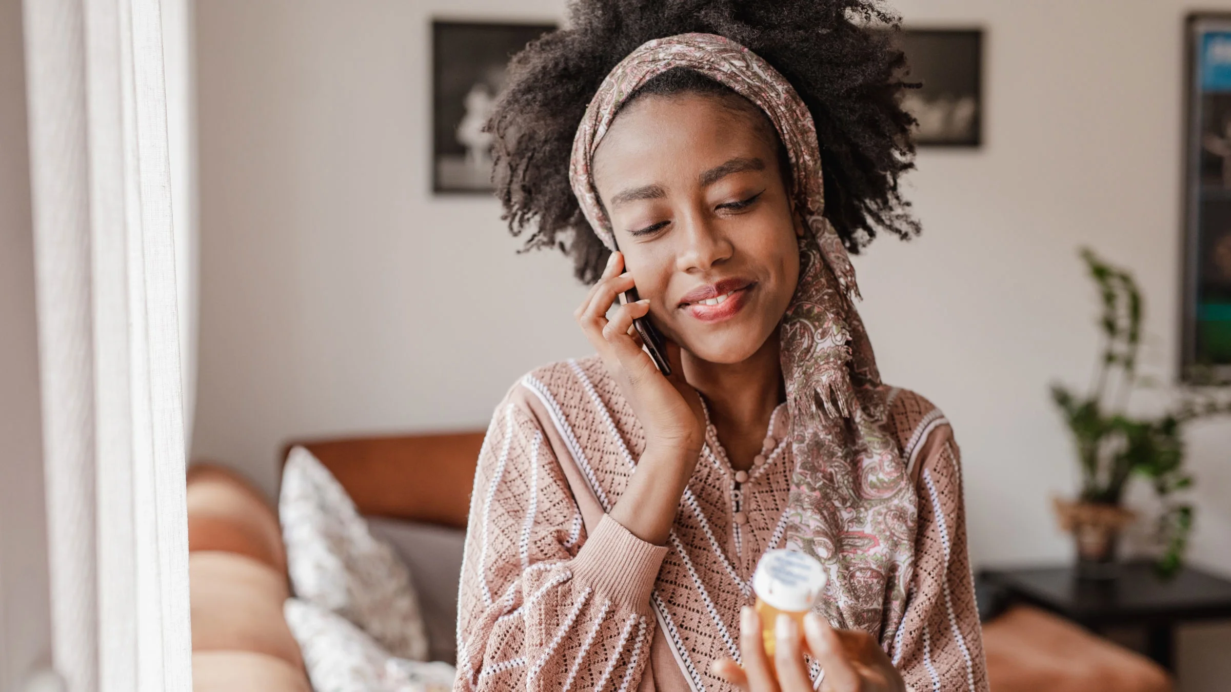 Woman is making a phone call while holding a bottle of medicine in her hand.