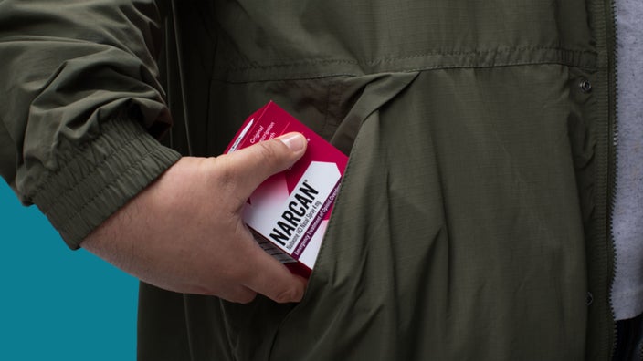 A hand places a box of Narcan in a coat pocket.