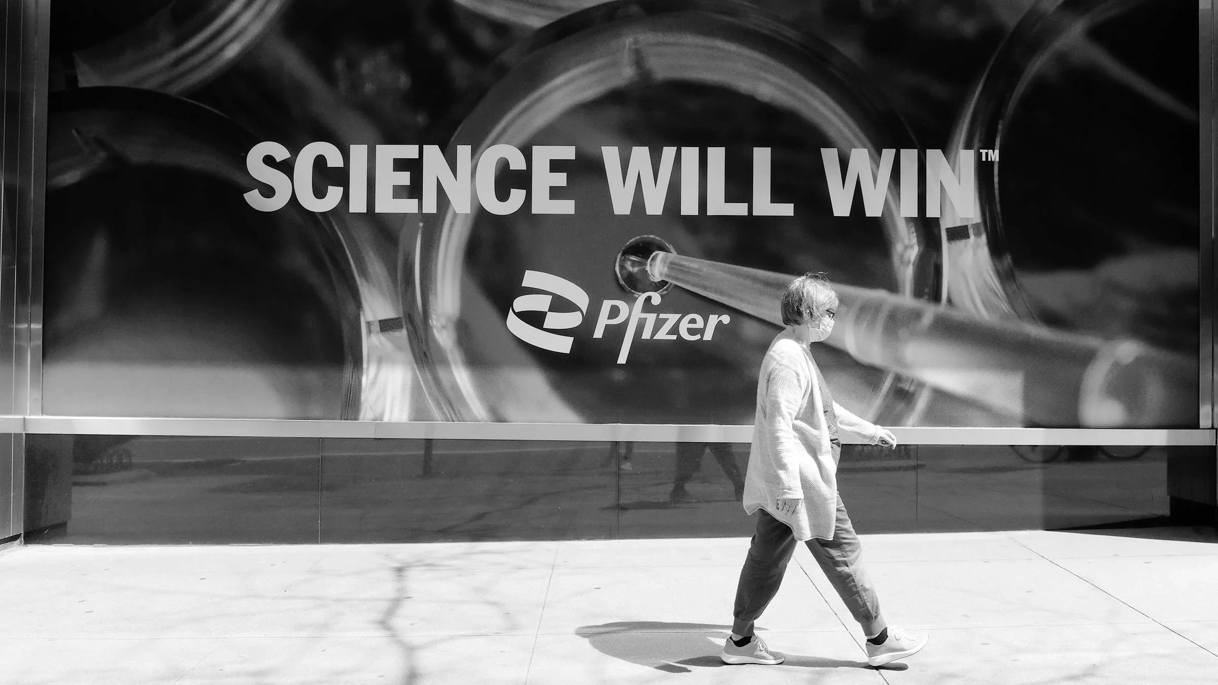 Woman walking by a wall billboard reading "SCIENCE WILL WIN - Pfizer" on the street.