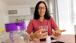 A woman sits at a dining table and takes medicine with a glass of water at home.
Dusan Stankovic/E+ via Getty Images 