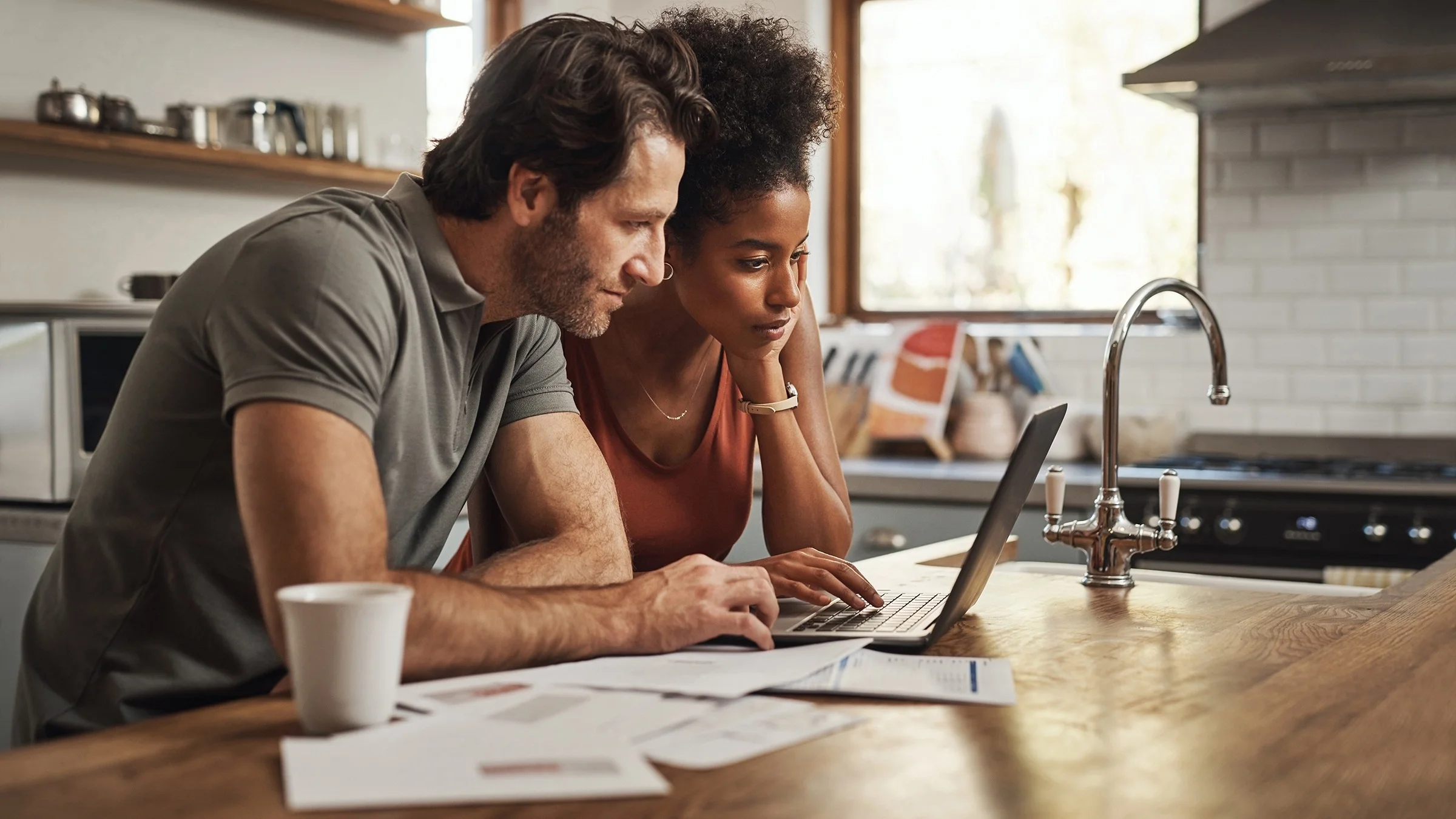 Couple reviewing paperwork for taxes on their laptop together in the kitchen.