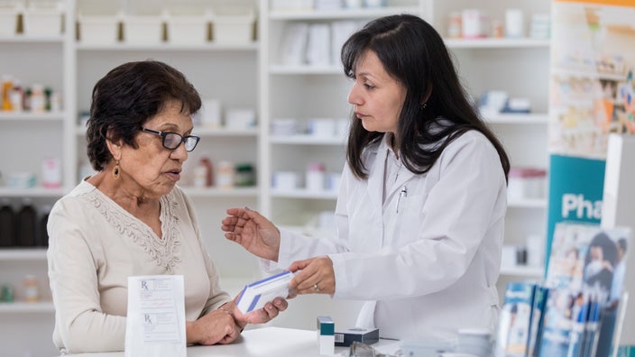Elderly woman looking at a prescription box with her pharmacist at the counter.