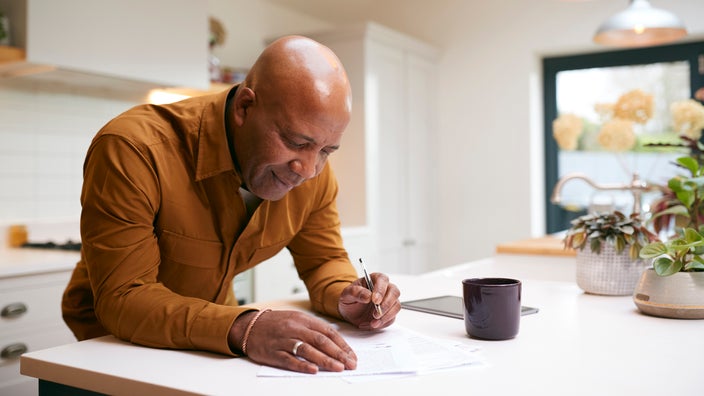 Older man reviewing and writing paperwork at his kitchen counter.