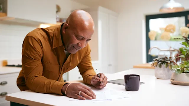 Health: Health Insurance: man reviewing paperwork at kitchen counter 1282868220