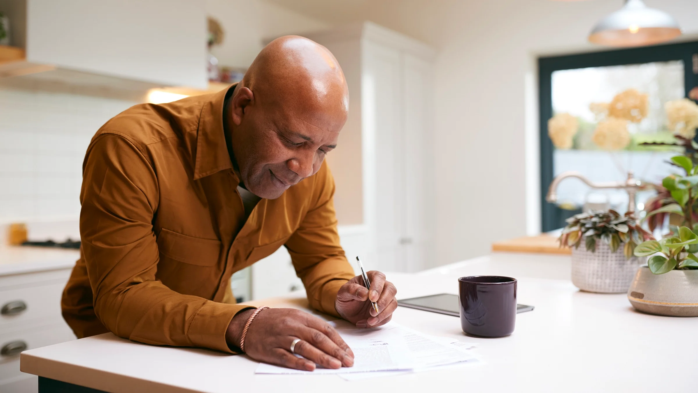 Older man reviewing and writing paperwork at his kitchen counter.