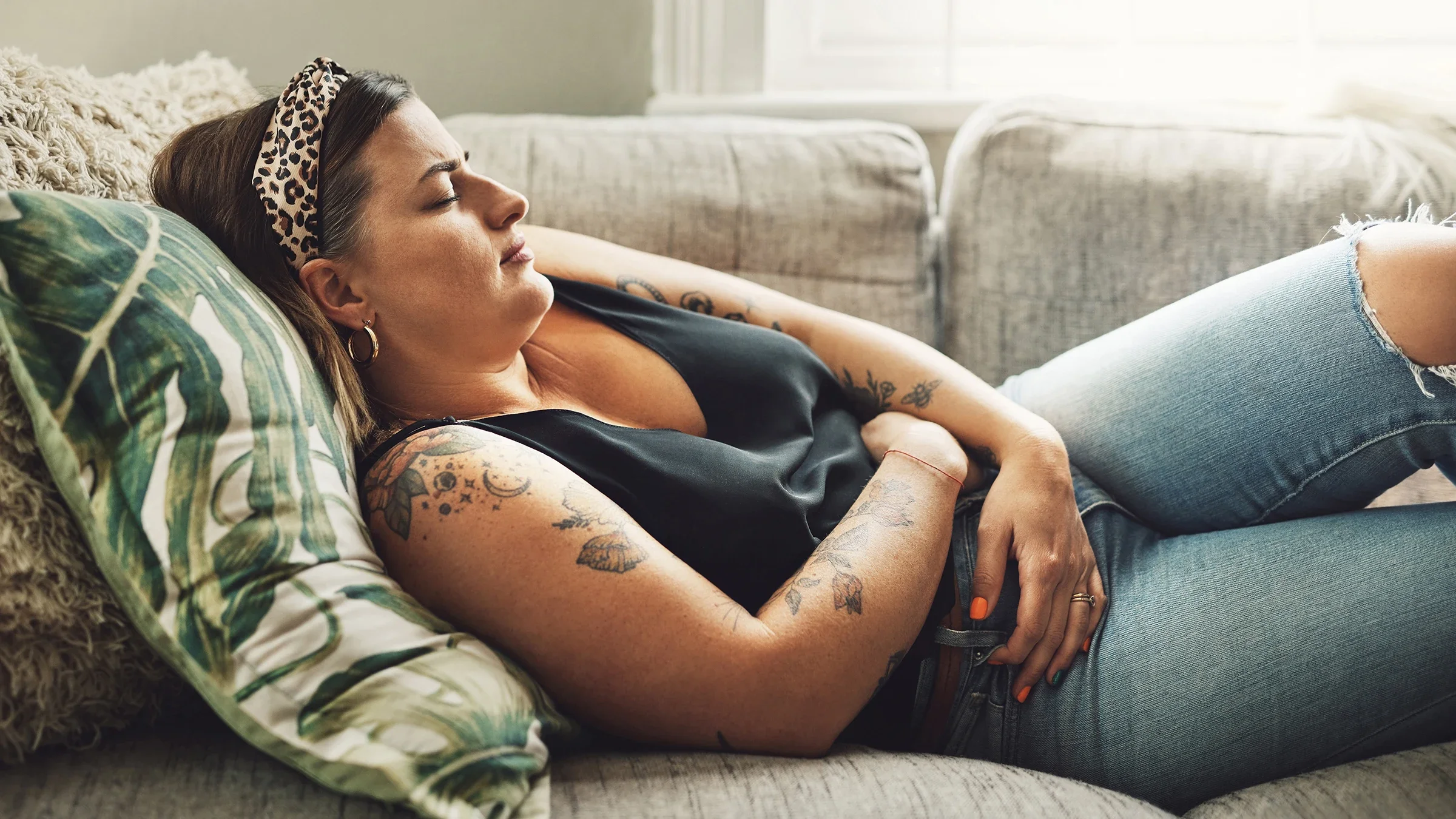 Woman laying down on couch grasping her stomach in pain.
PeopleImages/iStock via Getty Images