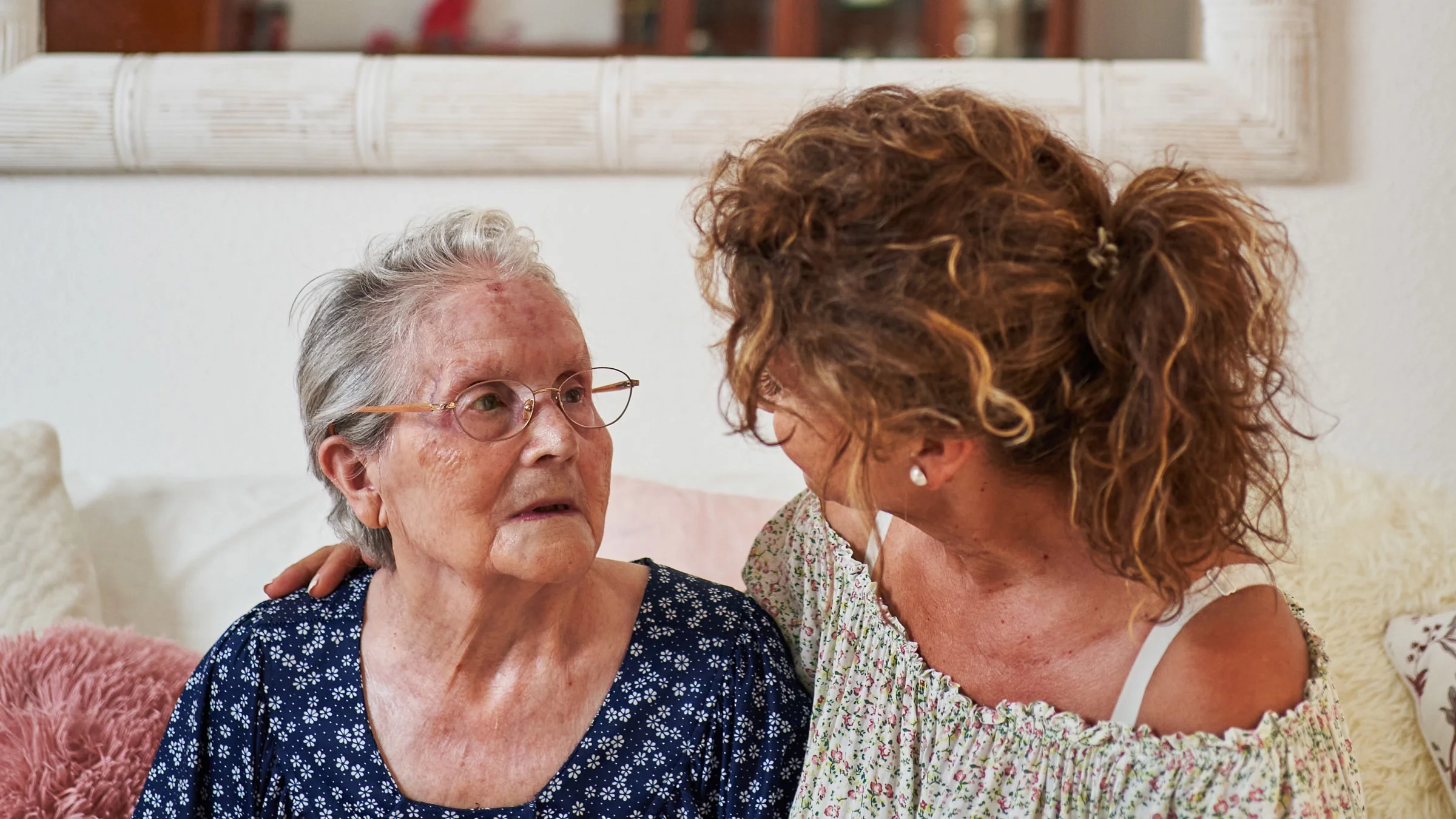 A middle-aged adult having a conversation with an elderly relative on a couch.