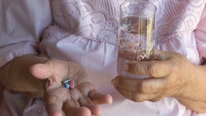 A person holds three pills in one hand and a glass of water in the other hand.