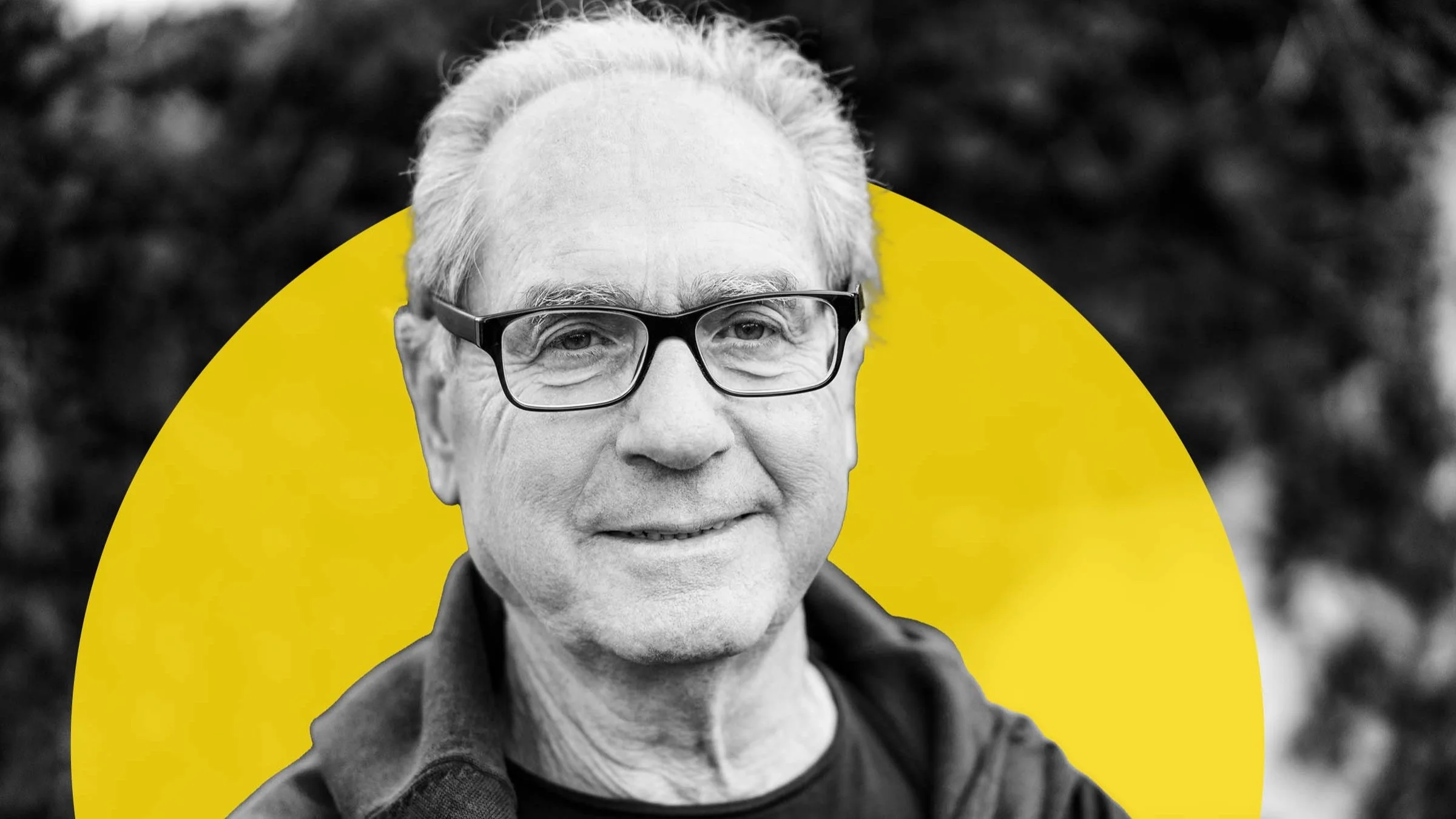 Black and white portrait of a man with a receding hairline. He is wearing black rectangular glasses and there is an added graphic yellow circle behind his head.