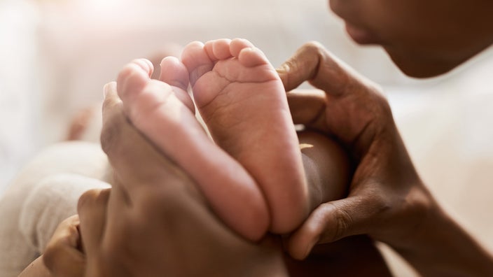 Close-up on a mother holding her newborns feet together. You can see the bottom of the mother's face in the corner, her chin and lips.