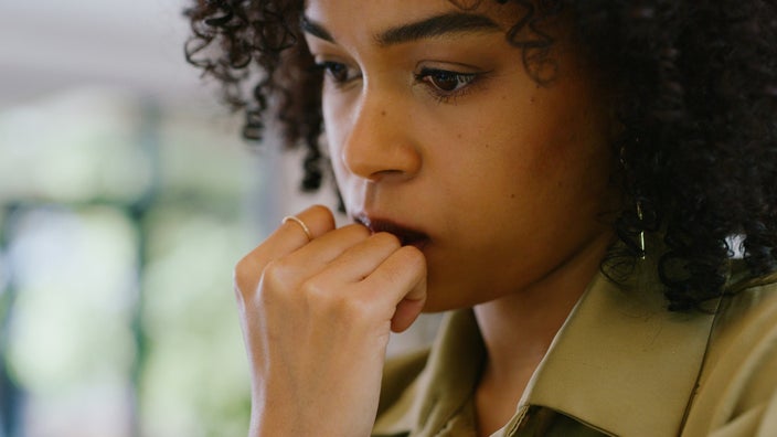 Close-up of a woman with dark, curly hair looking at her computer. She looks worried or nervous.